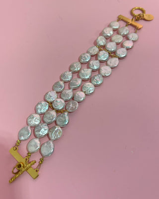Bracelet with teardrop-shaped pearls and gold clasps on a pink background