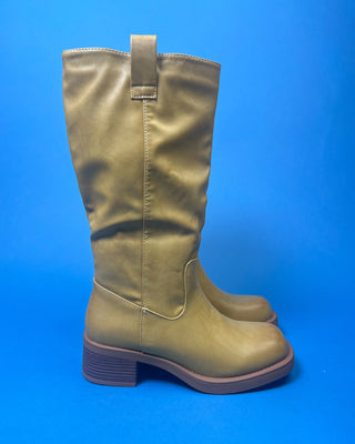 A tan leather knee-high boot with a brown stacked heel, held up against a solid blue background.