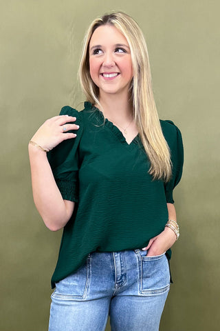 Woman wearing a green top and blue jeans against a green background