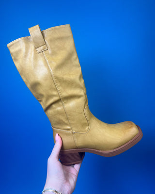 A tan leather knee-high boot with a brown stacked heel, held up against a solid blue background.