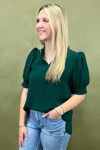 Woman wearing a green blouse with puffed sleeves against a green background