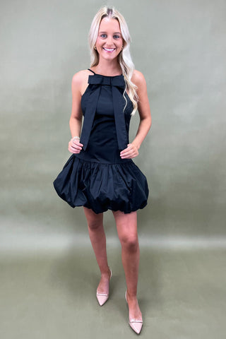 Woman wearing a black dress with a bow detail on a plain background