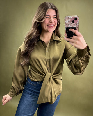Woman taking a selfie wearing an olive green shirt and blue jeans on a green background