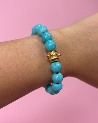 Turquoise beaded bracelet with a gold clasp on a wrist against a pink background