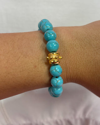Turquoise beaded bracelet with a gold accent on a wrist against a white background