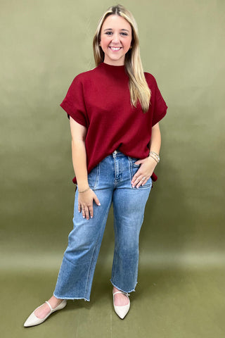 Woman wearing a red top and blue jeans against a green background