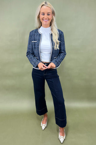 Woman wearing a blue checkered jacket and dark pants against a green background