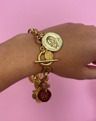 Gold charm bracelet on a wrist against a pink background