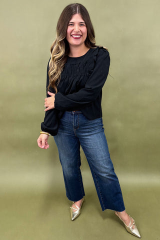 Woman wearing a black top and blue jeans against a green background
