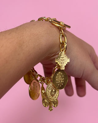 Gold bracelet with charms held against a pink background