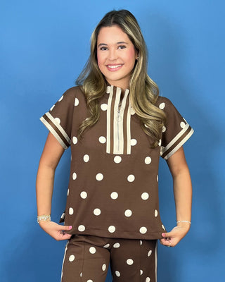 A woman modeling a brown short-sleeve top and matching pants set with white polka dots and cream trim