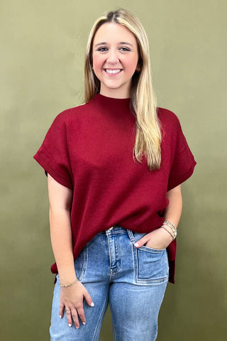 Woman wearing a red sweater and blue jeans against a green background