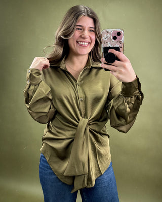 Woman taking a selfie wearing an olive green shirt and blue jeans on a green background