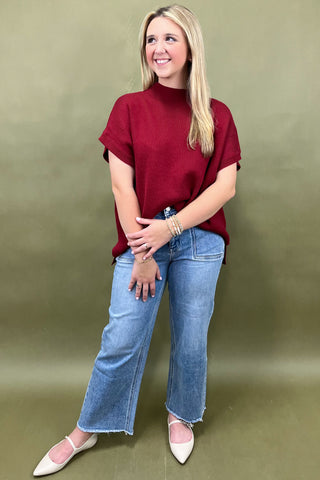 Woman wearing a red top and blue jeans against a green background