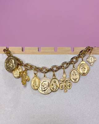 Gold charm bracelet with various charms on a pink and gray background