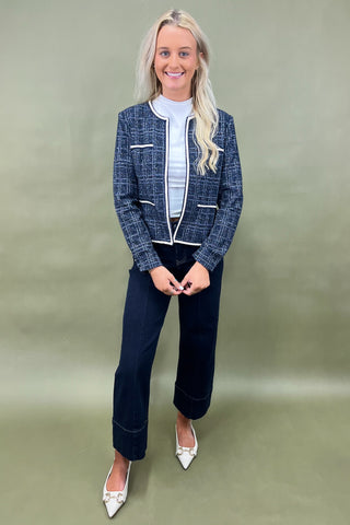 Woman wearing a blue checkered jacket and dark pants against a green background
