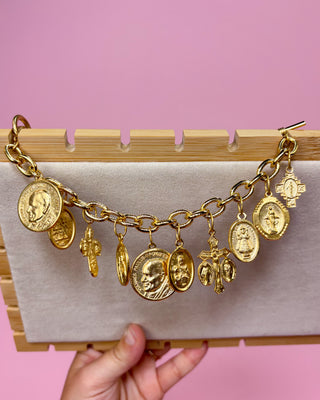 Gold charm bracelet with various charms on a pink background