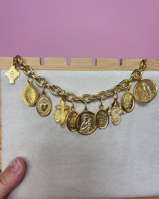 Gold charm bracelet with various charms on a pink background