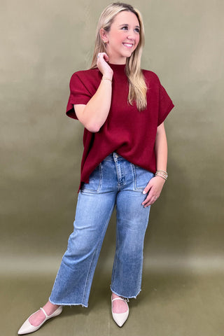 Woman wearing a red top and blue jeans against a beige background