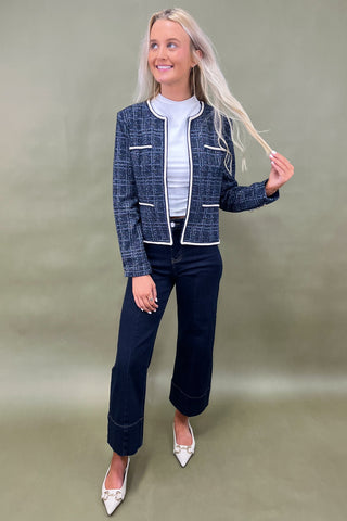 Woman wearing a blue checkered jacket and dark pants against a green background