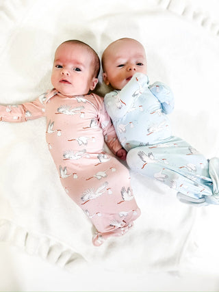 Two babies swaddled in patterned wraps on a white surface