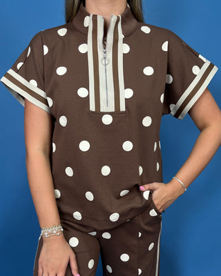 A woman modeling a brown two-piece lounge set with white polka dots, featuring a short-sleeve top with cream trim and matching wide-leg pants