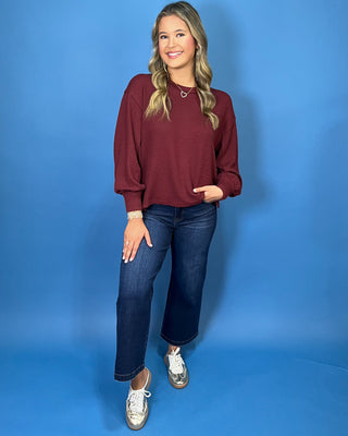Burgundy textured long sleeve sweater top with a crew neckline, relaxed fit, and banded cuffs.