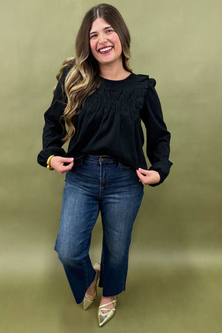 Woman wearing a black top and blue jeans against a green background