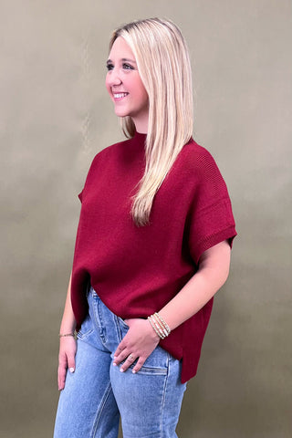 Woman wearing a red sweater and blue jeans against a beige background