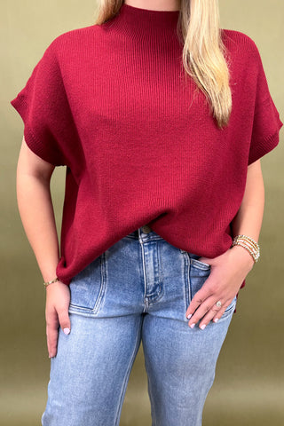 Person wearing a red sweater and blue jeans against a beige background