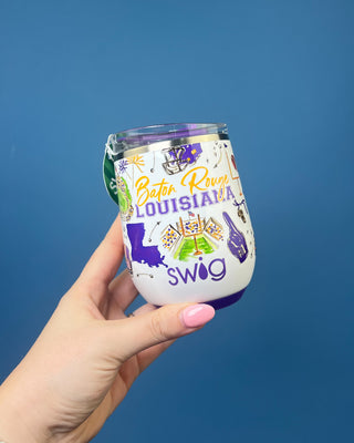 A hand with pink nail polish holds a white insulated stainless steel tumbler featuring Louisiana Bats Roush graphics, including purple and yellow text and illustrations, against a solid blue background.