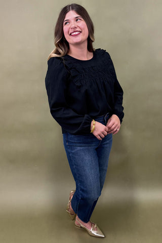 Woman wearing a black top and blue jeans against a green background