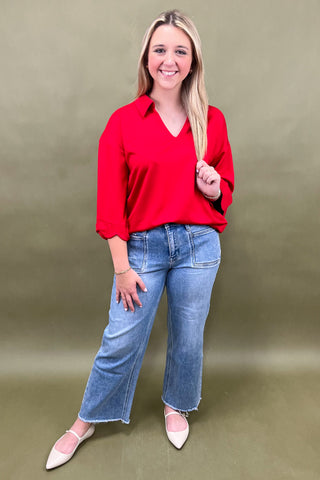Woman wearing a red blouse and blue jeans against a green background