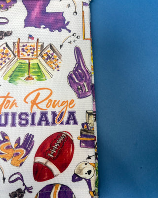 Swig Life Tailgates In Baton Rouge cotton kitchen towel featuring Baton Rouge football, stadium, helmets, footballs, and purple and gold game day illustrations.