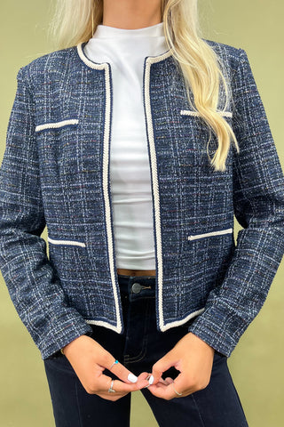 Woman wearing a blue checkered jacket and dark pants against a green background