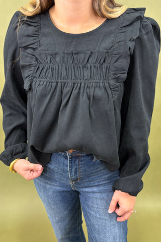 Person wearing a dark gray blouse with ruffled details and blue jeans on a yellow background