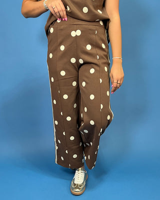 A person wearing brown wide-leg pants with large white polka dots and a matching brown sleeveless to