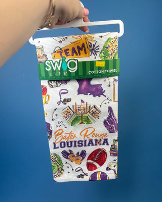 Swig Life Tailgates In Baton Rouge cotton kitchen towel featuring Baton Rouge football, stadium, helmets, footballs, and purple and gold game day illustrations.
