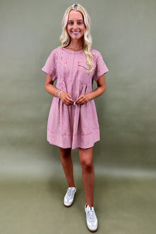 Woman wearing a pink and white checkered dress with white sneakers against a green background