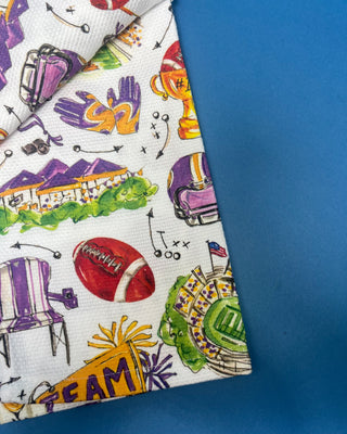 Swig Life Tailgates In Baton Rouge cotton kitchen towel featuring Baton Rouge football, stadium, helmets, footballs, and purple and gold game day illustrations.