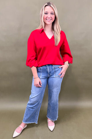 Woman wearing a red blouse and blue jeans against a plain background
