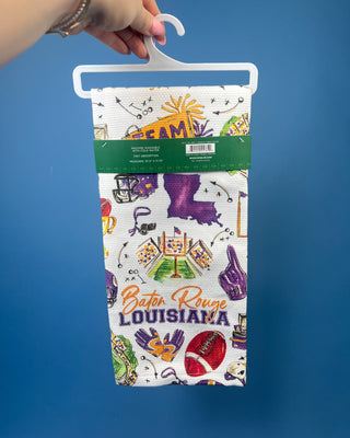 Swig Life Tailgates In Baton Rouge cotton kitchen towel featuring Baton Rouge football, stadium, helmets, footballs, and purple and gold game day illustrations.