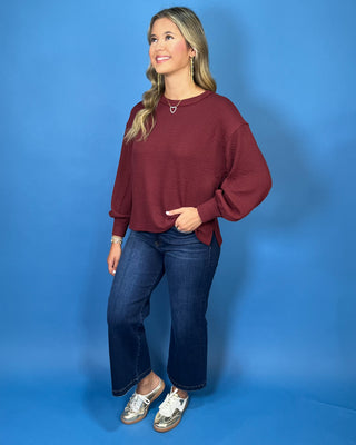 Burgundy textured long sleeve sweater top with a crew neckline, relaxed fit, and banded cuffs.