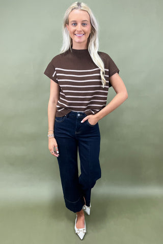 Woman wearing a brown and white striped top with blue jeans against a plain background