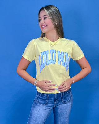 A woman posing in a light yellow graphic t-shirt with blue lettering, paired with blue jeans