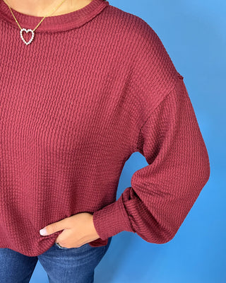 Burgundy textured long sleeve sweater top with a crew neckline, relaxed fit, and banded cuffs.