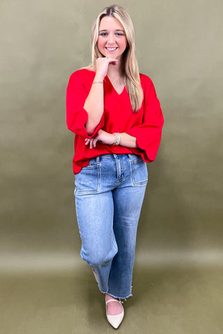 Woman wearing a red top and blue jeans against a beige background