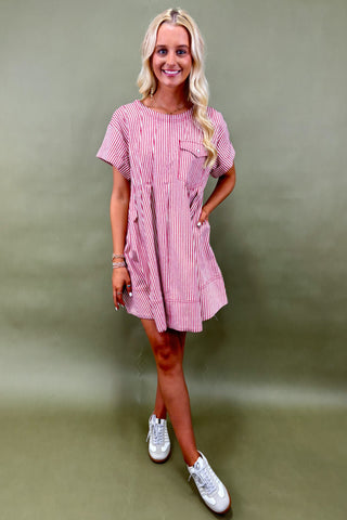 Woman wearing a pink and white striped dress with white sneakers against a green background