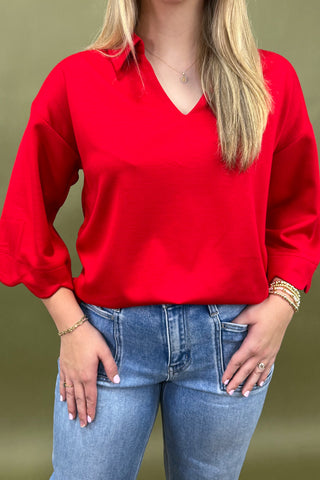 Person wearing a red blouse and blue jeans against a green background