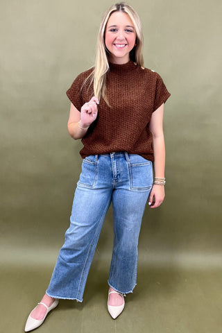 Woman wearing a brown sweater and blue jeans against a green background